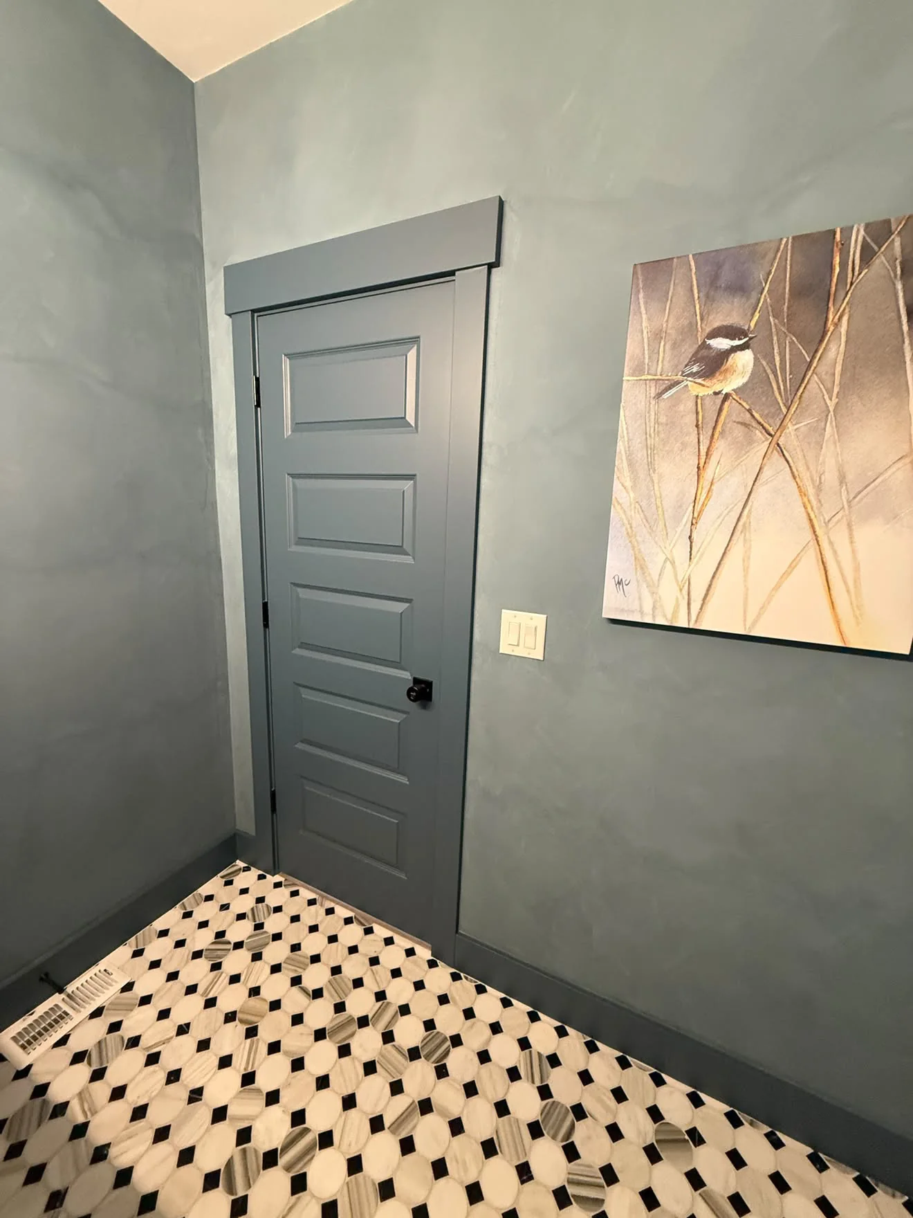 A powder room in slate blue plaster, carried over the walls and the door casing, above a black and white mosaic floor